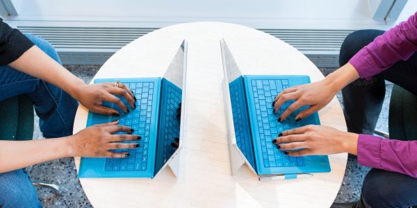 Vue de dessus de deux personnes travaillant face à face sur des ordinateurs portables bleus, autour d'une table ronde blanche